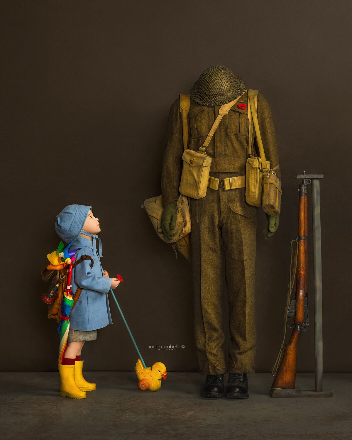 Small child dressed in vintage clothing, holding vintage toys, looking up at WWII uniform in admiration. 
