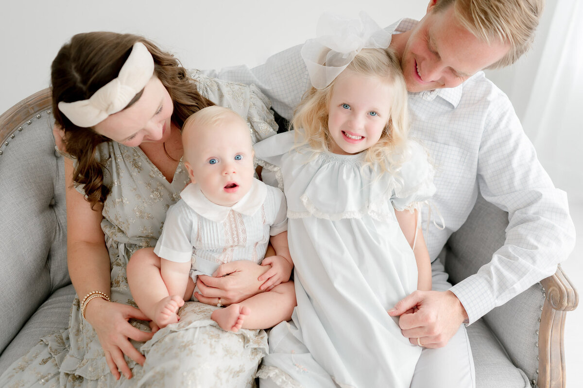 A baby boy and his sister smile as their parents hold them