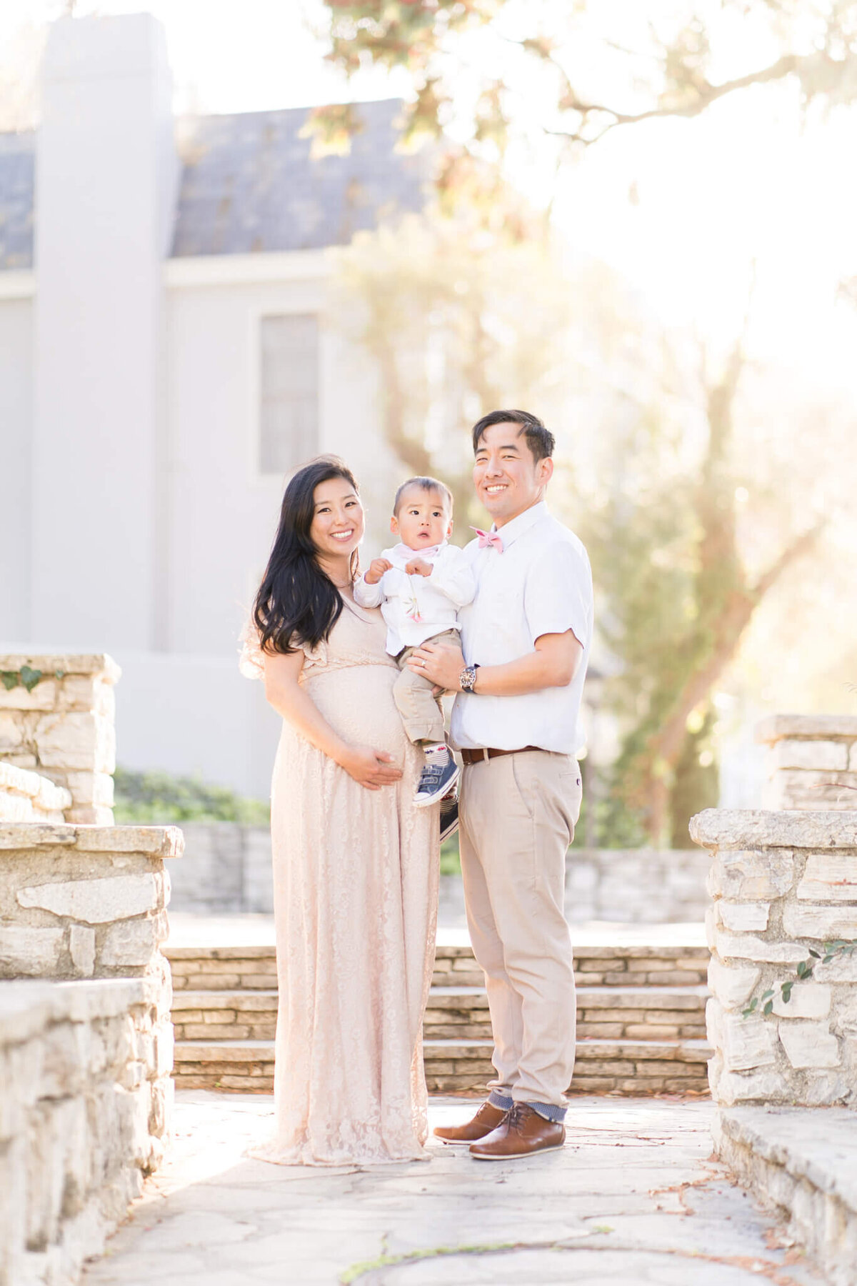 Asian family standing on brick pathway by a mansion holding son in the middle.