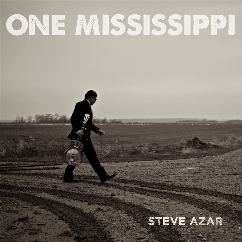 Steve Azar Single Cover Title One Mississippi singer walking in long shot across dirt road wearing black suit carrying his guitar
