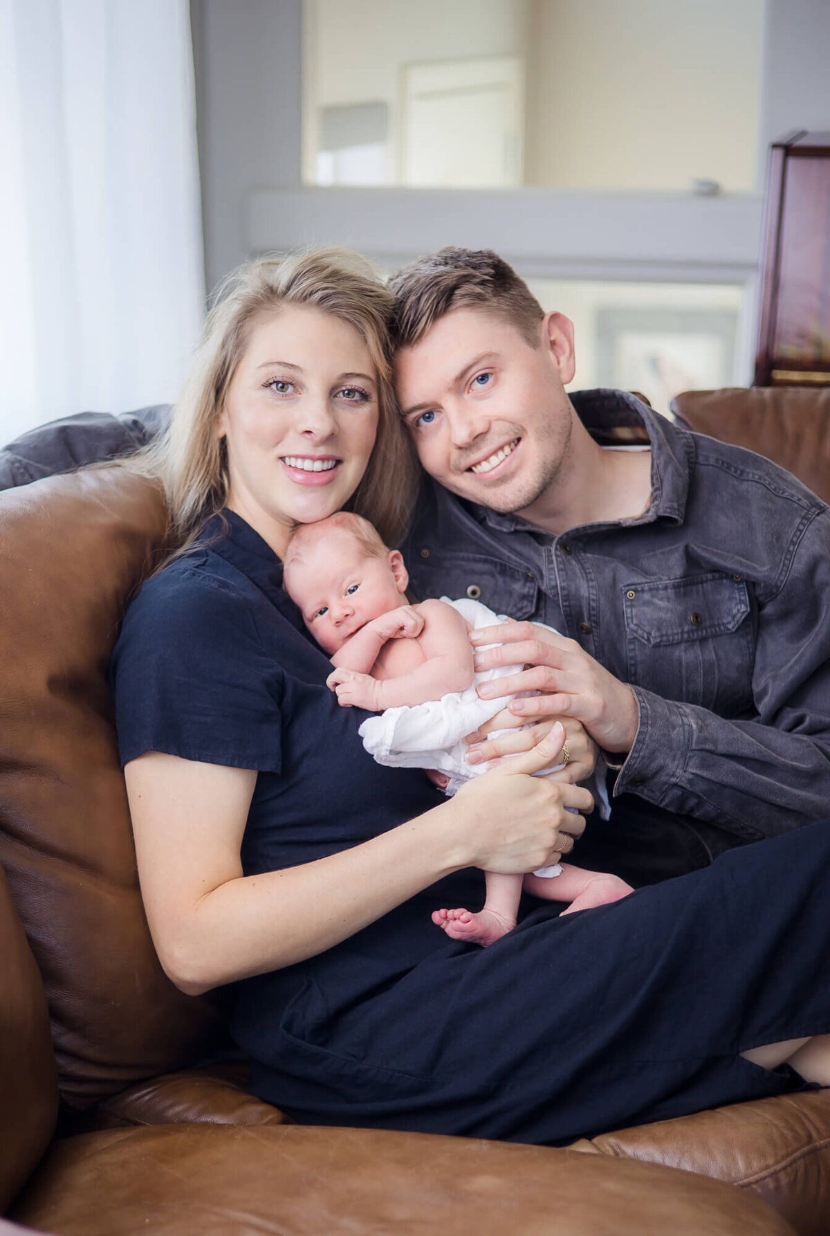 blonde couple snuggling their newborn son on the couch during their las vegas newborn photography session