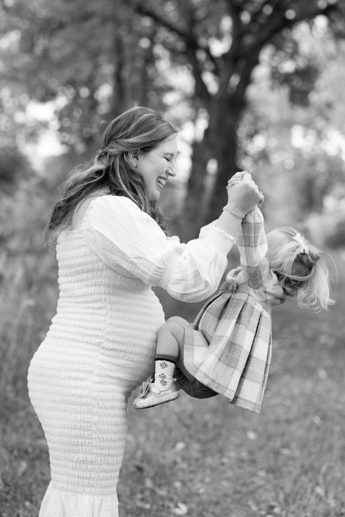 Black and white image of a mom smiling at and picking up her toddler daughter.