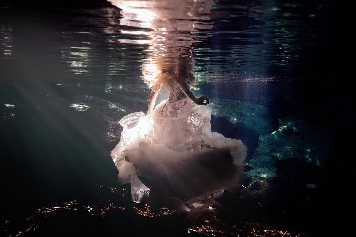 Bride walking in chest deep water from behind in wedding dress.