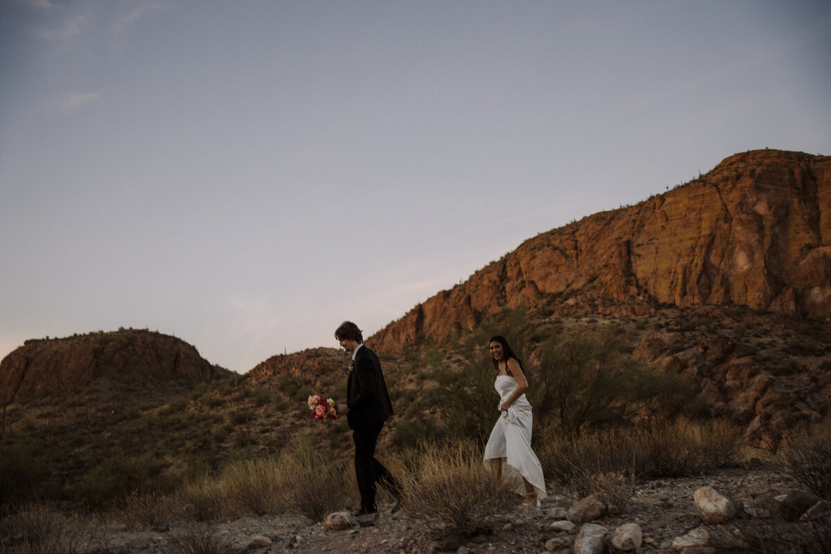 happy bride and groom walking in desert with mountain backdrop, destination wedding photography