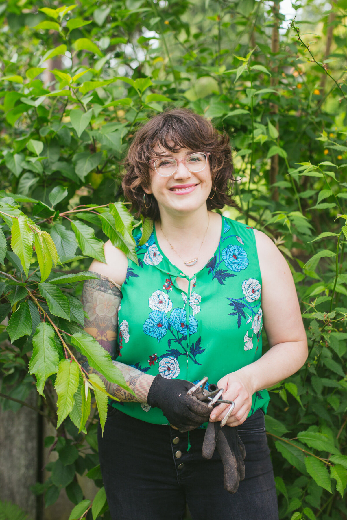 A woman standing next to bushes with her gardening gloves on.