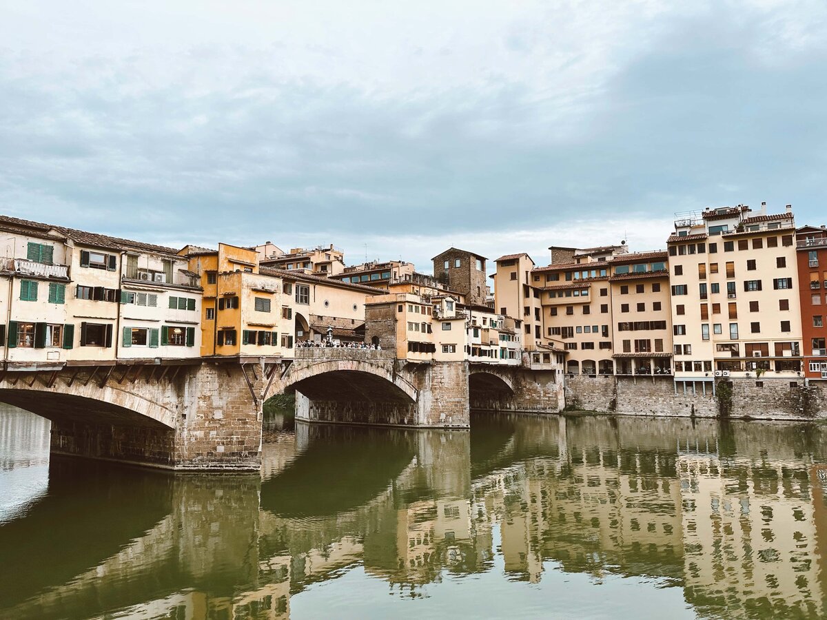old Ponte Vecchio bridge arching over green water with orange and beige buildings behind it. 