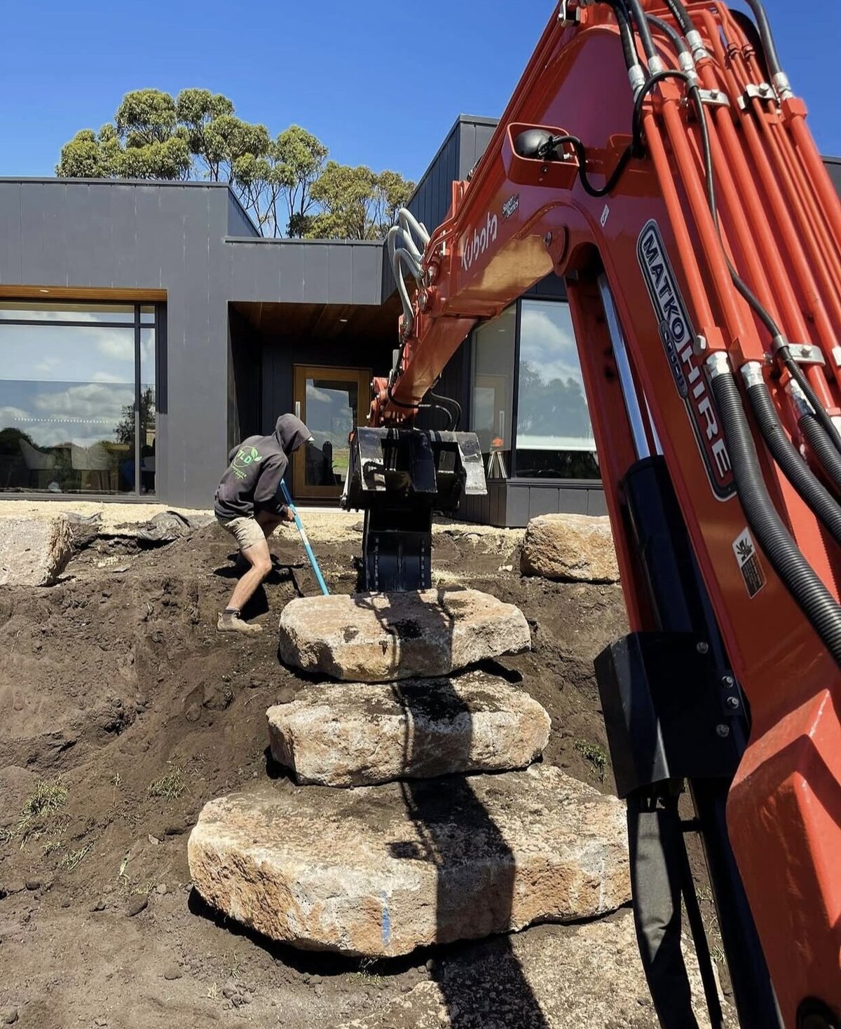 Man and machine working together with earthmoving and rock work for a landscape design in warrnambool