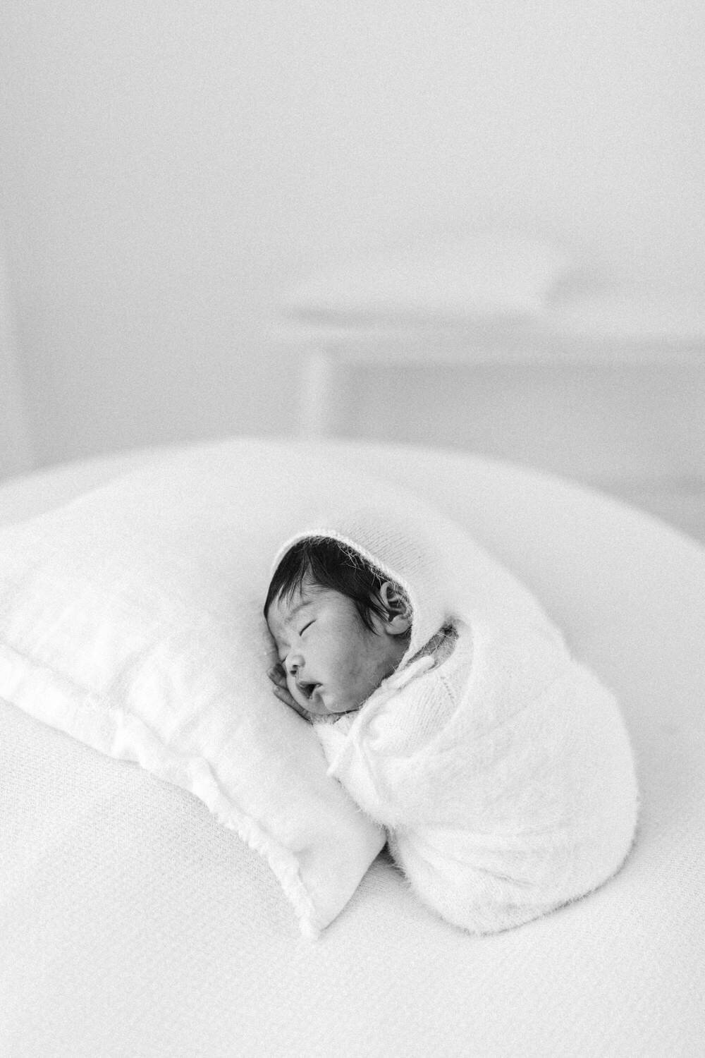 Newborn baby snuggles asleep on a pillow wearing a bonnet