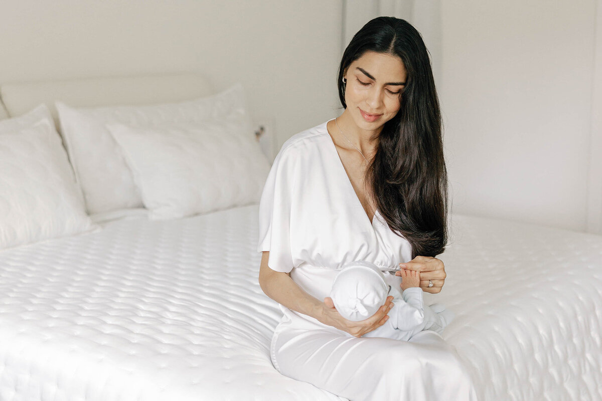 A mother cradles her newborn while sitting on a bed in soft natural light during a Florida Keys family portrait session.