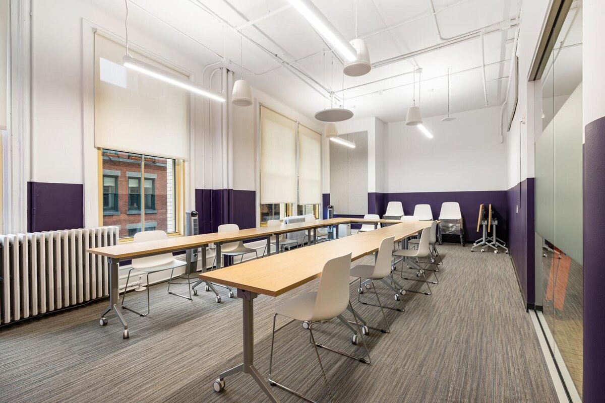 Large training room with long rolling tables, white chairs, and deep purple color blocking along the walls.