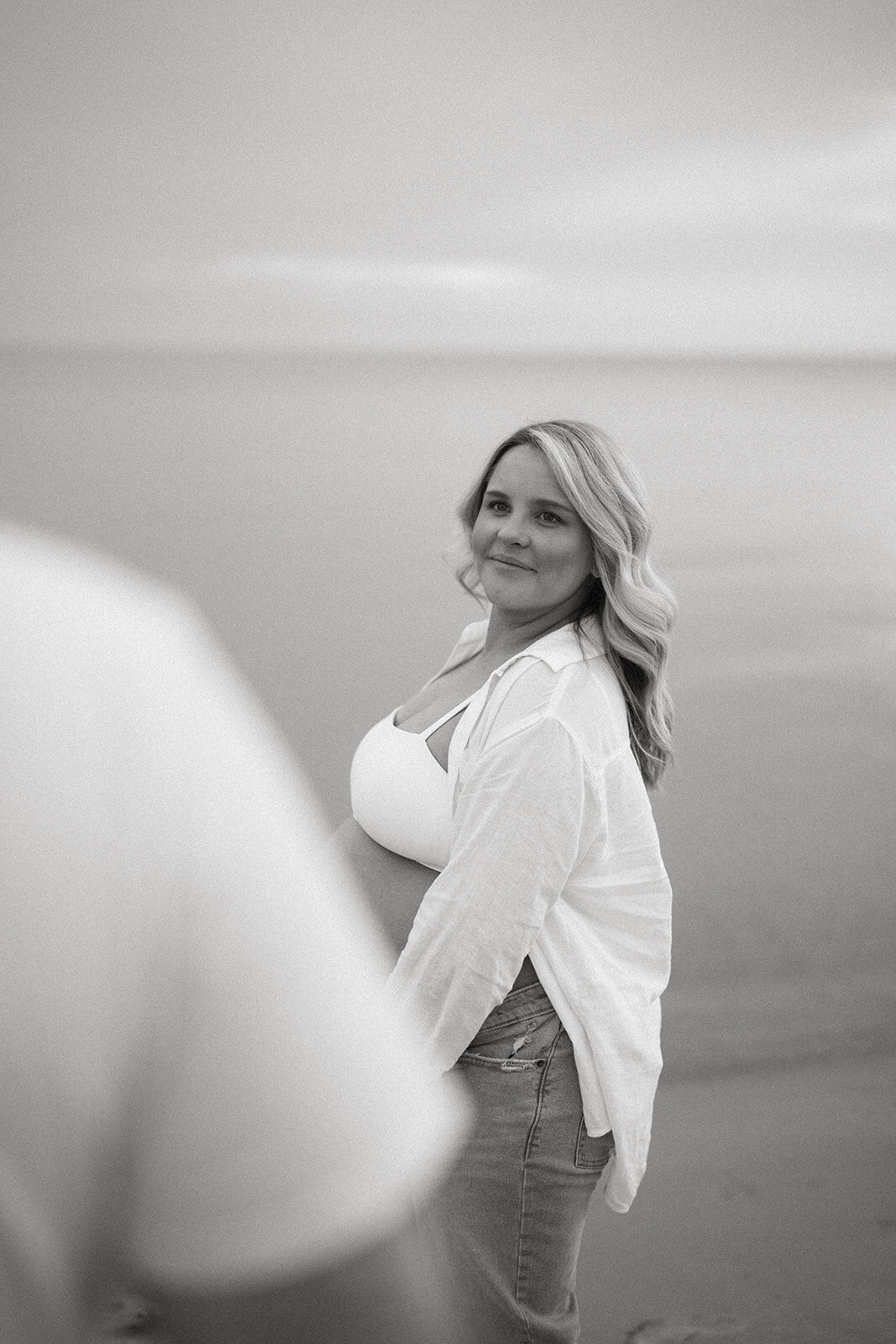 Black and white maternity photo of expecting mother looking over her shoulder at South Haven North Beach.