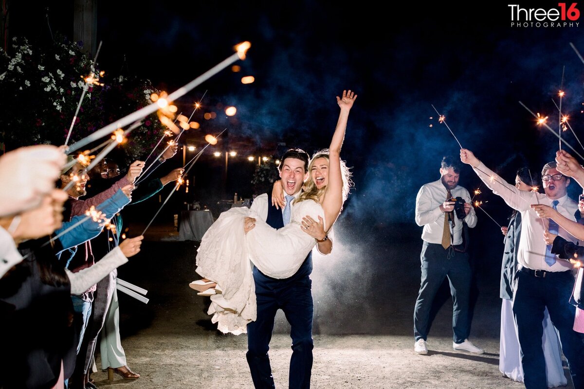 Groom carries his Bride out through a tunnel of sparklers held by wedding guests