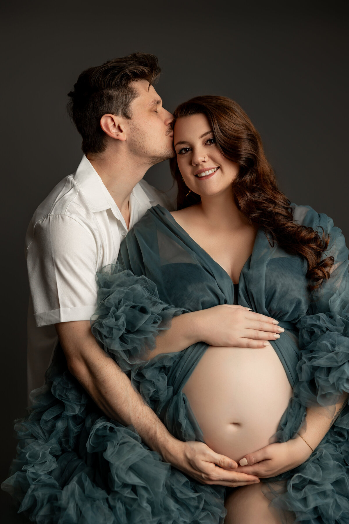 The expectant mother, wearing a green sheer dress, shares a close-up moment with her husband, both capturing the joy and excitement of their pregnancy. Captured by Inland Empire maternity photographer Kaitlyn Dawn Photography.