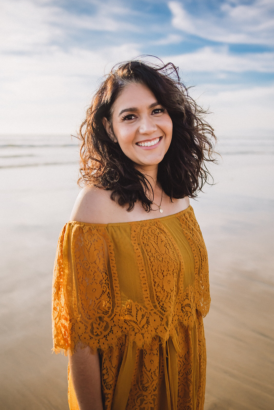 Woman in yellow dress smiles at a sunny Los Angeles beach.