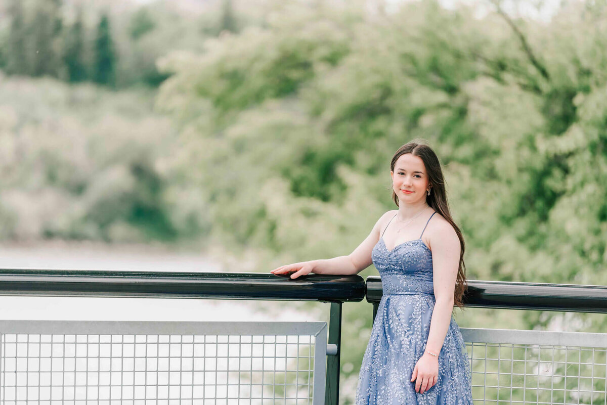 A young lady leaning  on a thick black railing over looking the south Saskatchewan river. 