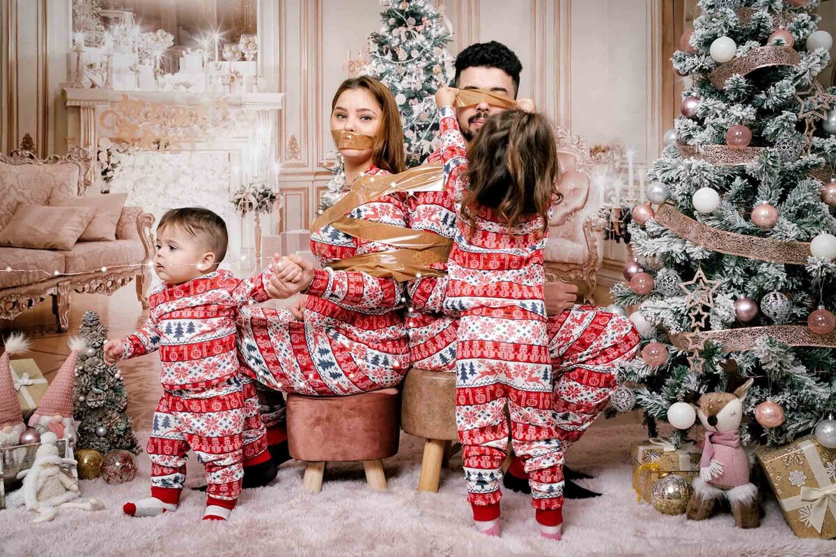 Family wearing matching Christmas pajamas opening gifts in Calini Weddings Studio - festive tree and joyful holiday atmosphere.