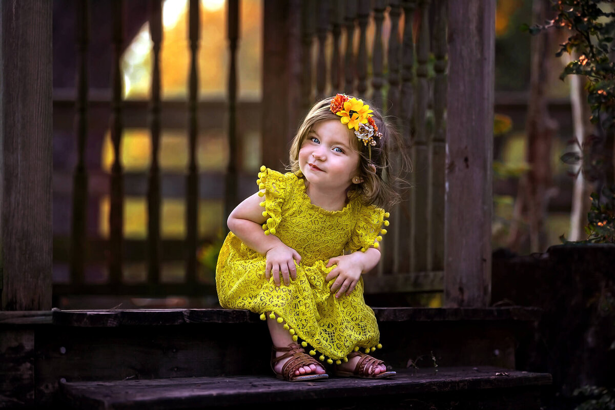 Adorable toddler wearing a bright yellow dress and smiling.