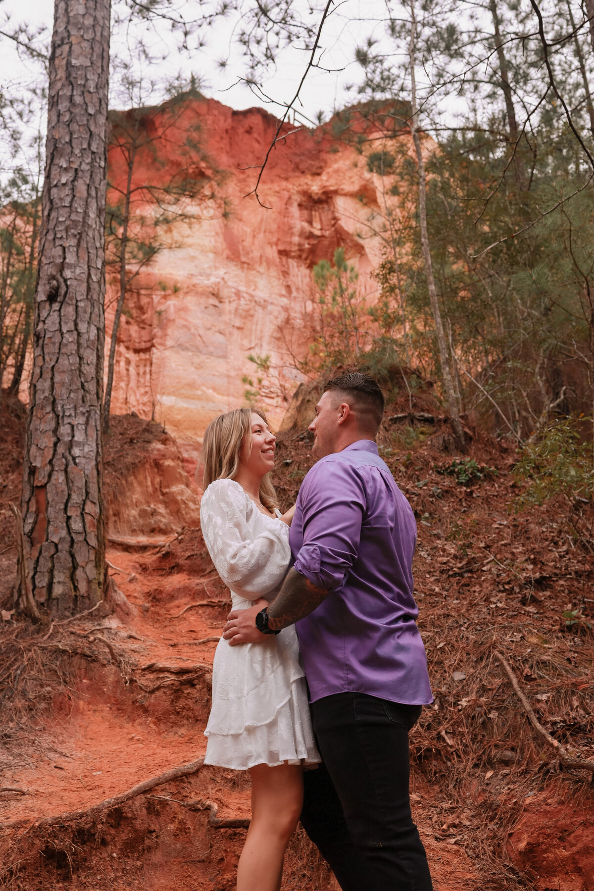 engaged couple looking at each other with red rock behind them at Providence Canyon State Park by Georgia wedding Photographer Amanda Richardson Photography