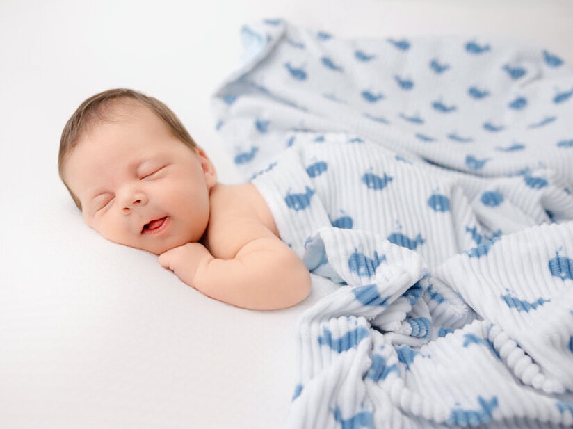 Smiling newborn boy with a white blanket with whales on it.
