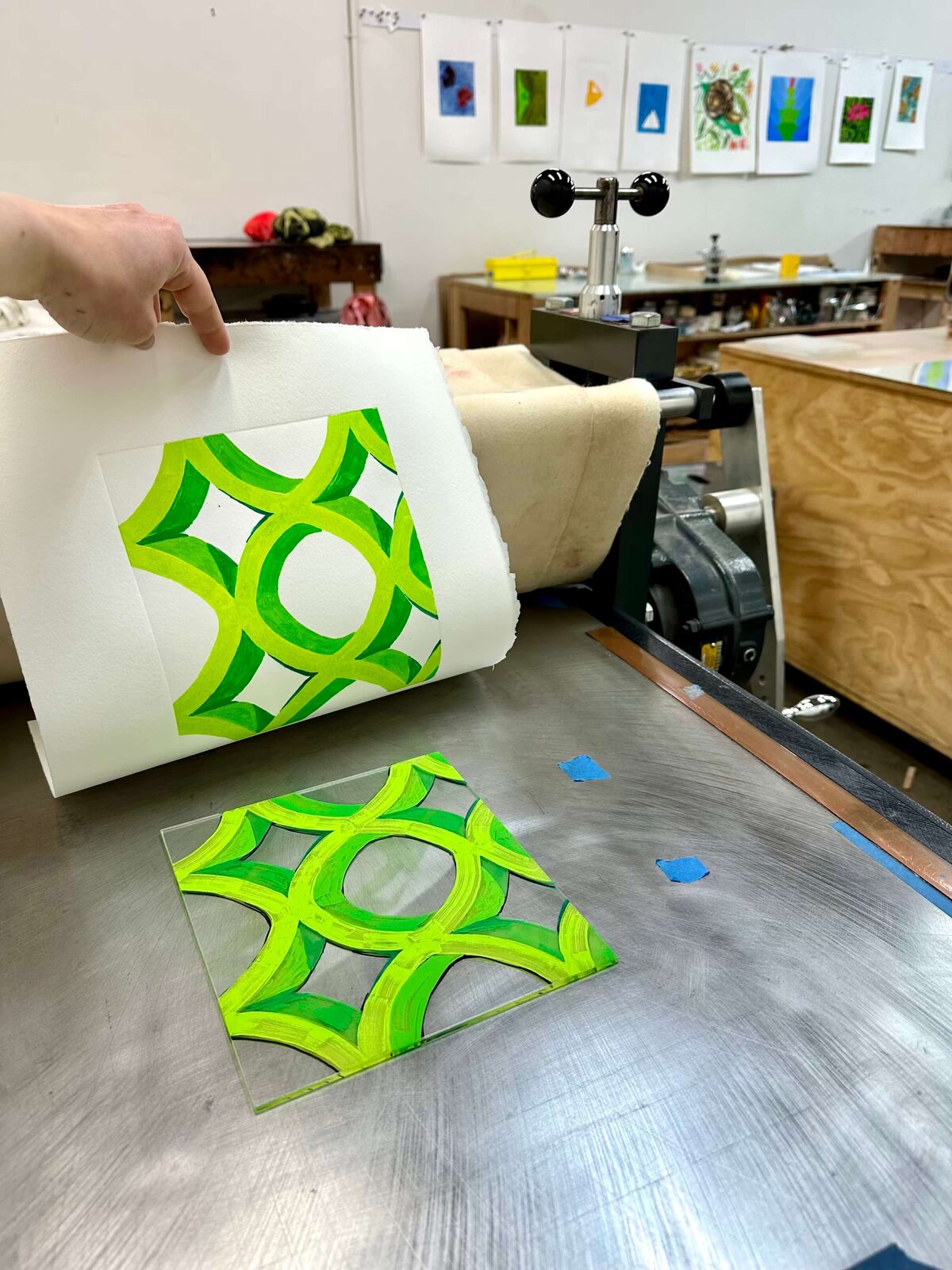 A vibrant green geometric monoprint being lifted from a plexiglass plate, capturing the crisp transfer and satisfying moment of reveal.