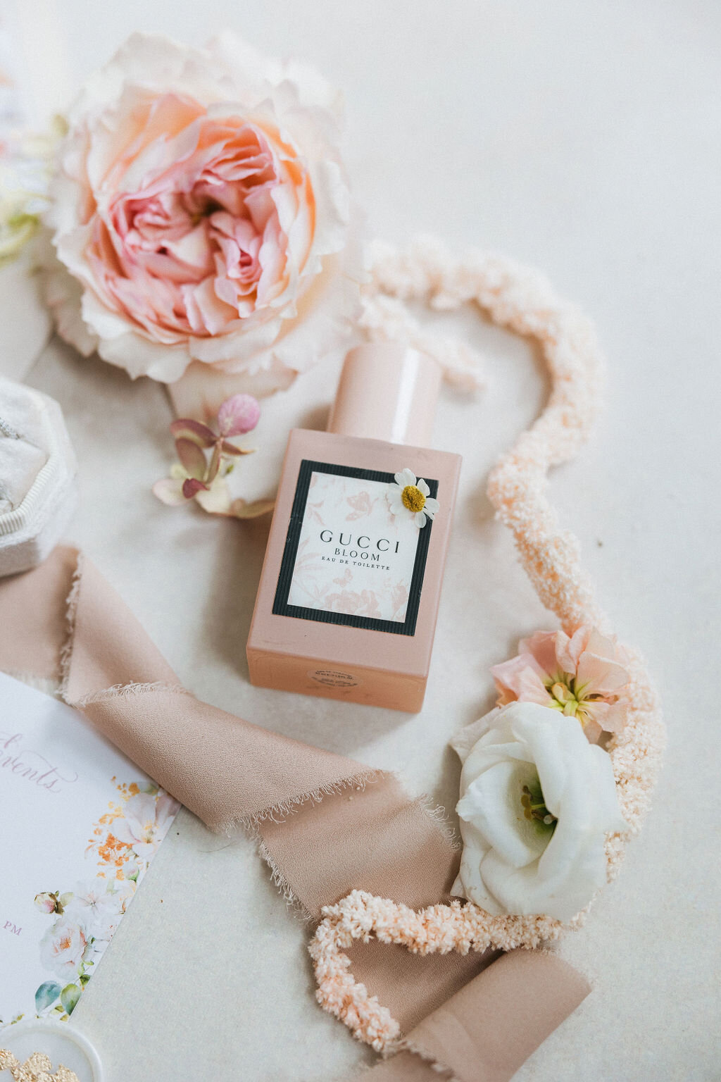 Gucci Bloom perfume bottle styled with blush silk ribbon, garden roses, and lisianthus—bridal detail from an Admiral House wedding in Charleston, captured by luxury wedding photographer Amia Marcell.
