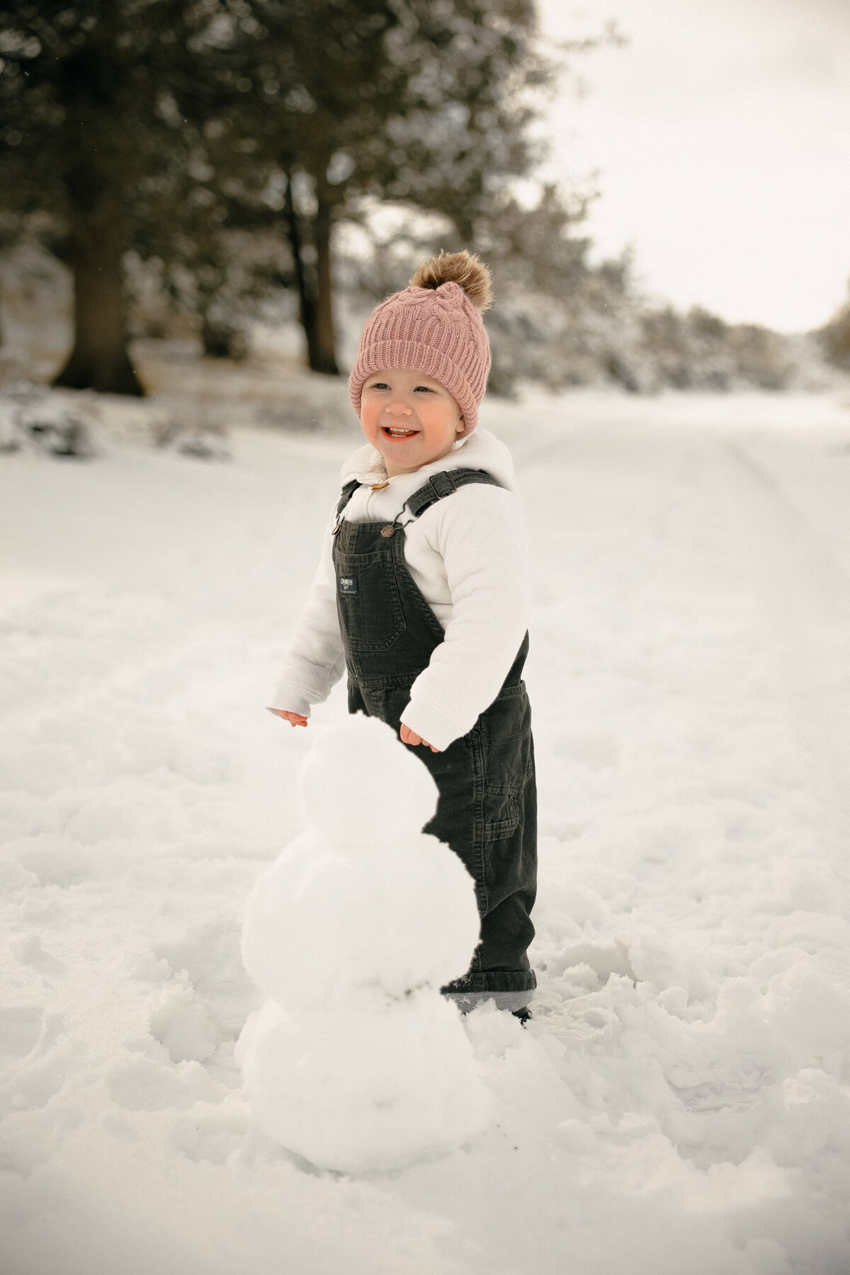 Toddler Building Snowman During Cozy Winter Family Session in Snowy Field
