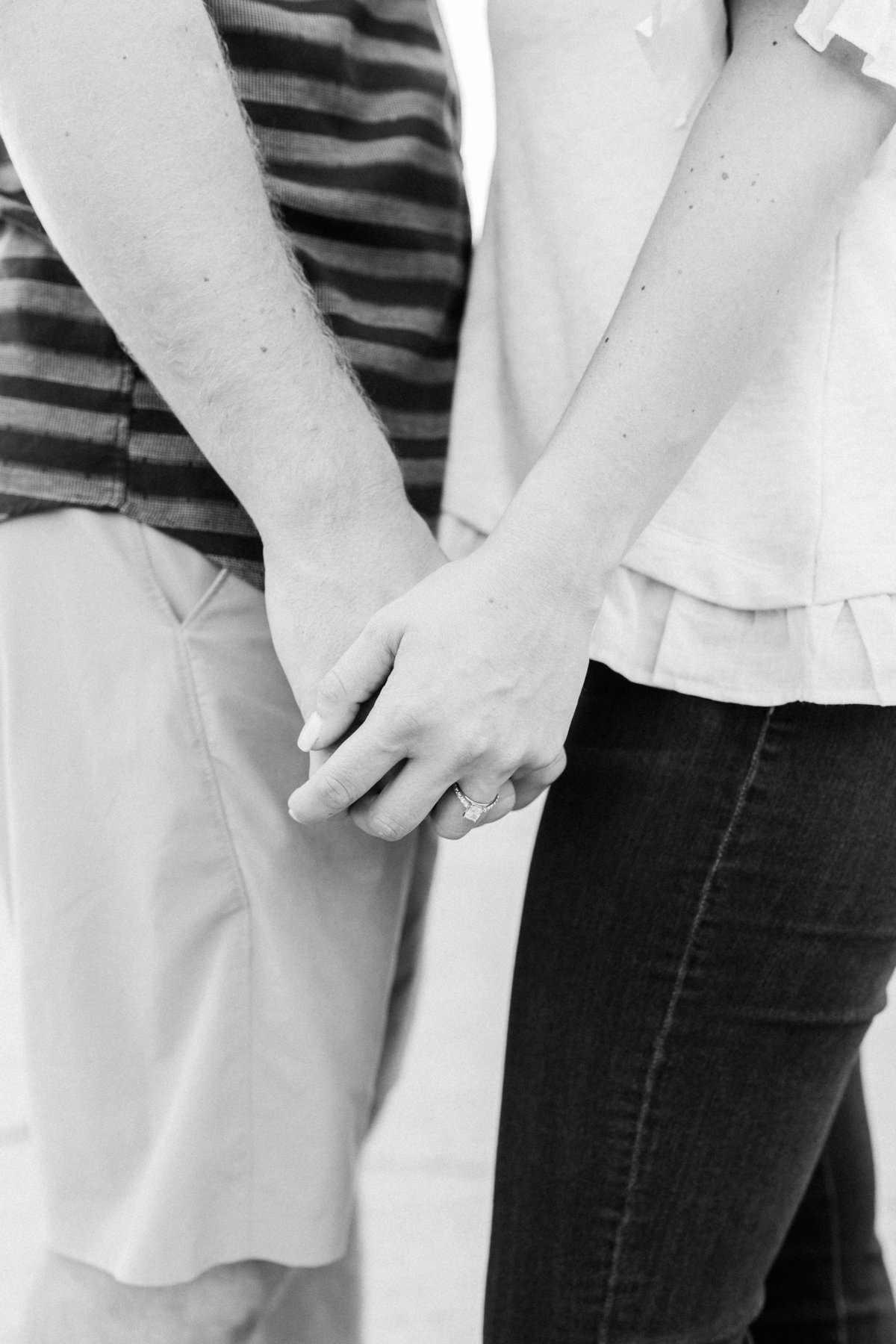 Close up black and white photo of a couples hands with a new shiny engagement ring showing