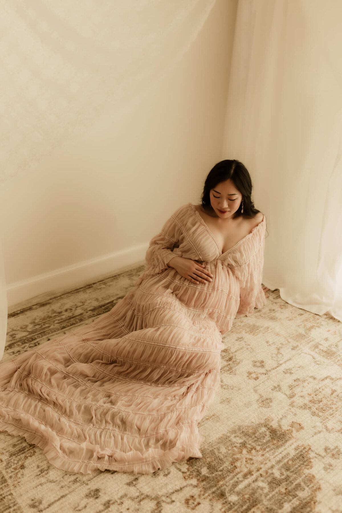 Maternity portrait of a mother wearing a blush dress while sitting on a rug, Edmond Oklahoma.