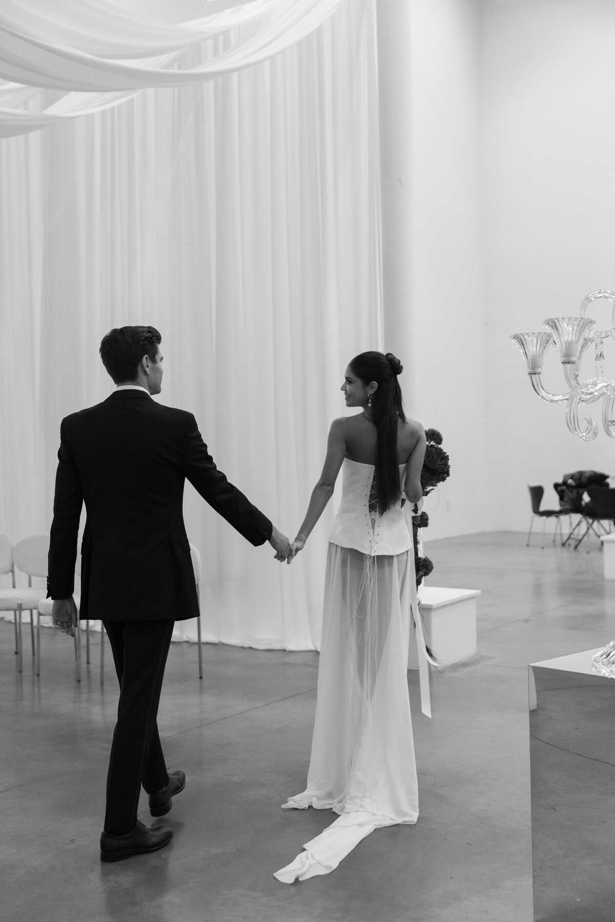 Couple walking hand in hand through a minimalist white wedding space.