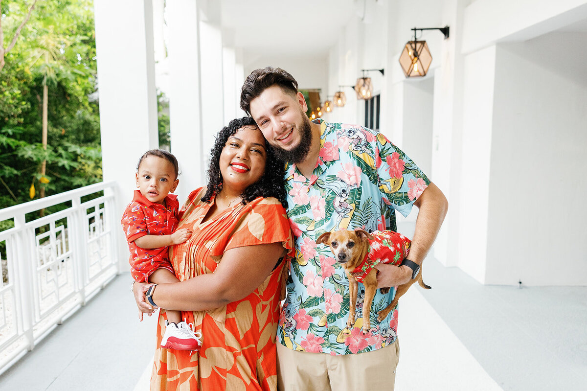 A cheerful family dressed in tropical-themed outfits poses with their baby and dog in a bright white hallway during a Florida Keys portrait session.