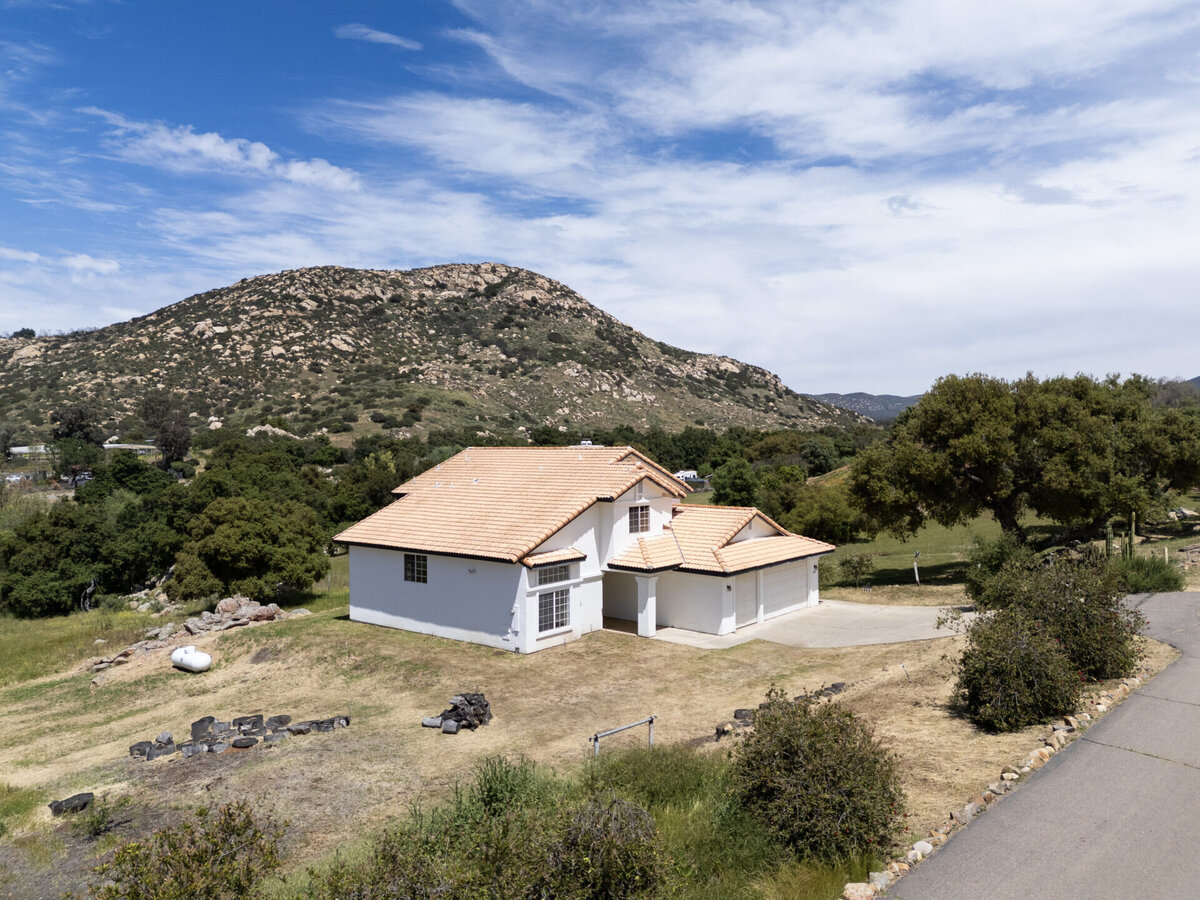Aerial of front of white home with mountains in the distance.