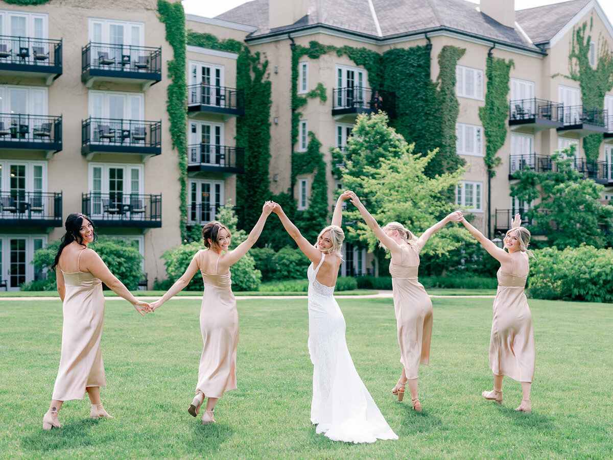 Bride and her bridesmaid hold hands and walk together and lift their arms as they celebrate