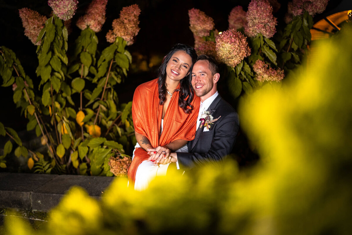 Night-time wedding photo of bride and groom sitting together and smiling in Phipps conservatory and botanical garden wedding venue.