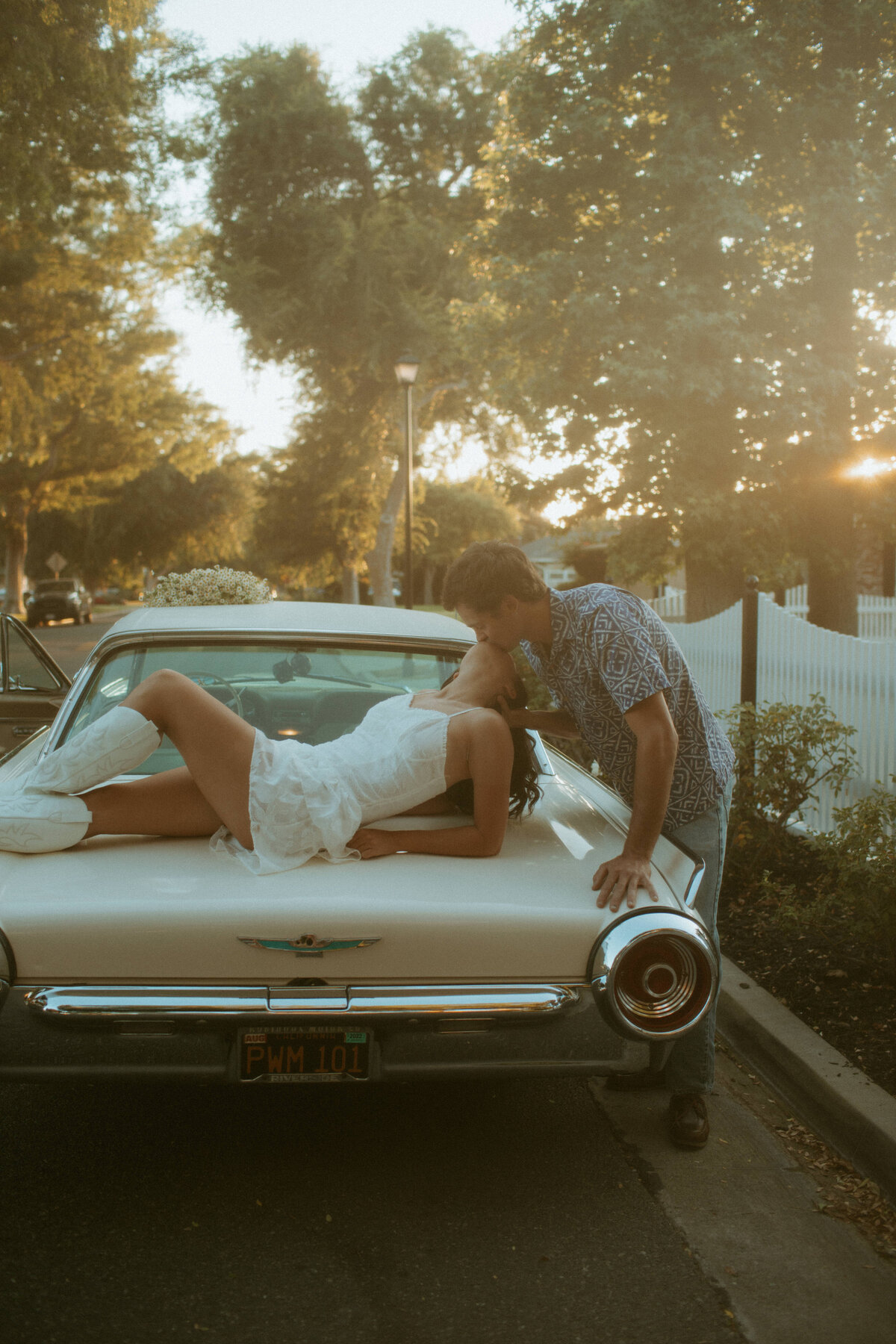 couples photos with classic car , shes laying on the back of car while hes leaning down to kiss her