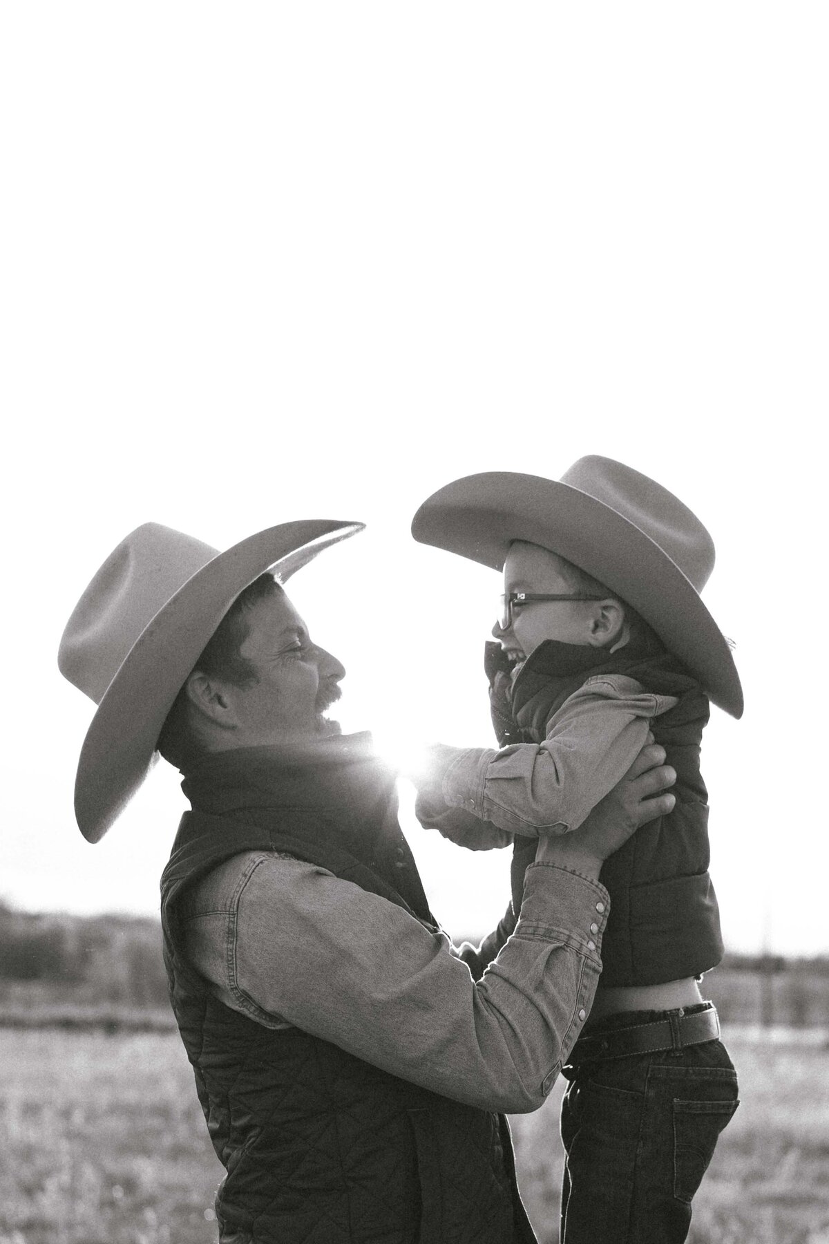 Father and son in cowboy hats during golden hour sharing laughter