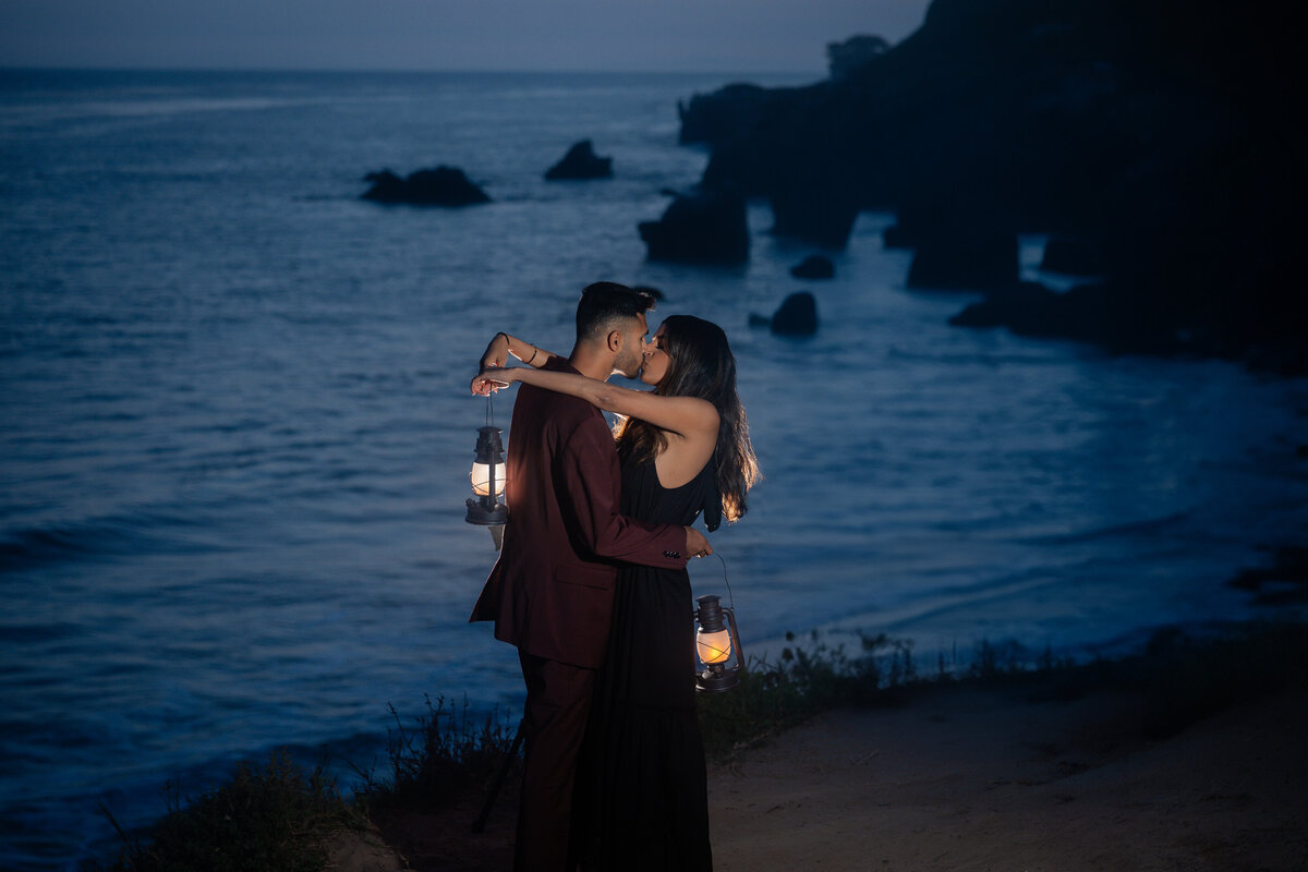Indian couple eloping at El Matador State Beach in Malibu during blue hour holding lanterns and kissing.