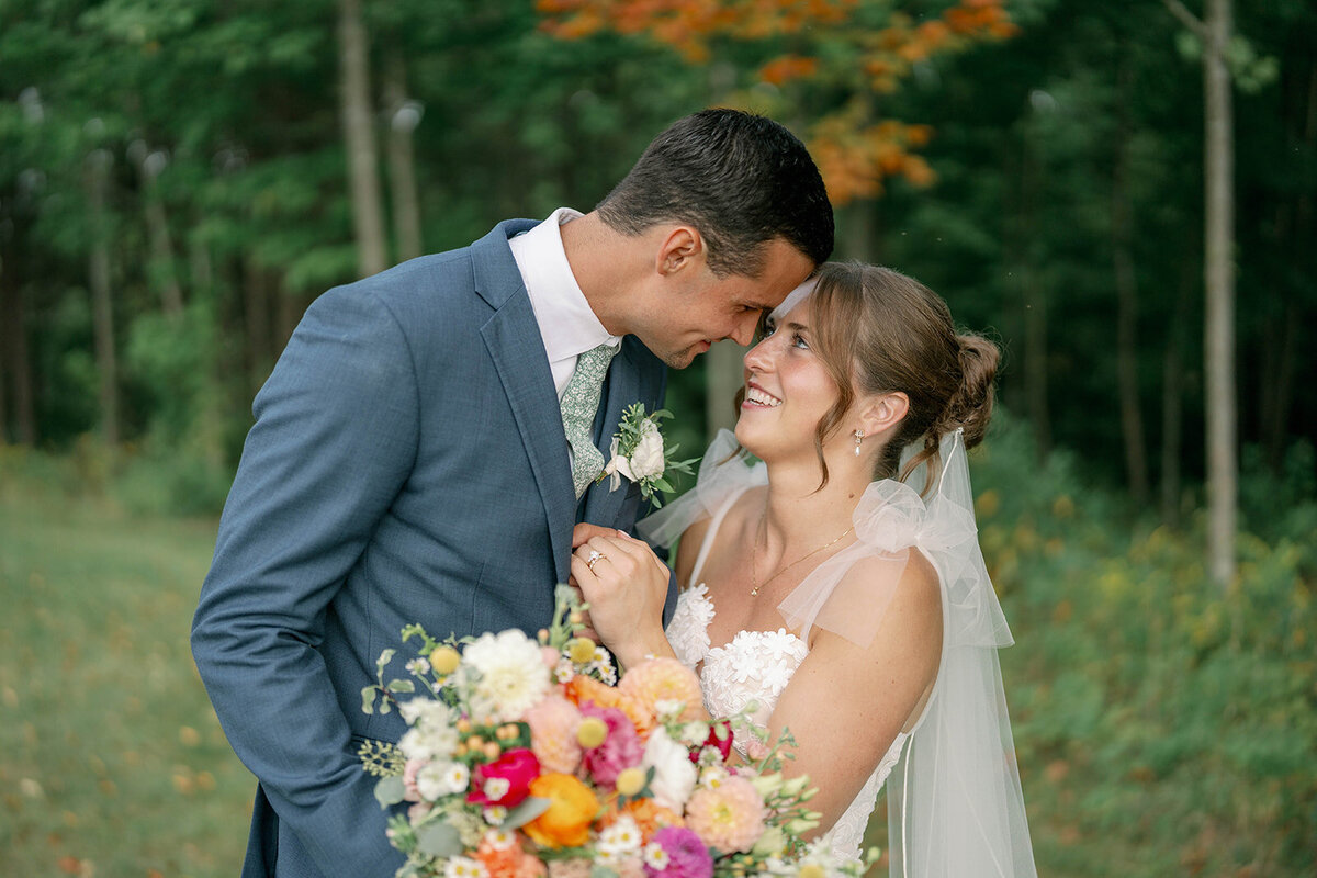 Bride and groom smiling with their foreheads touching during their September wedding at The Cherry Barn at Nugent Orchards in Frankfort, Michigan. A candid, romantic wedding portrait captured among the apple orchards.