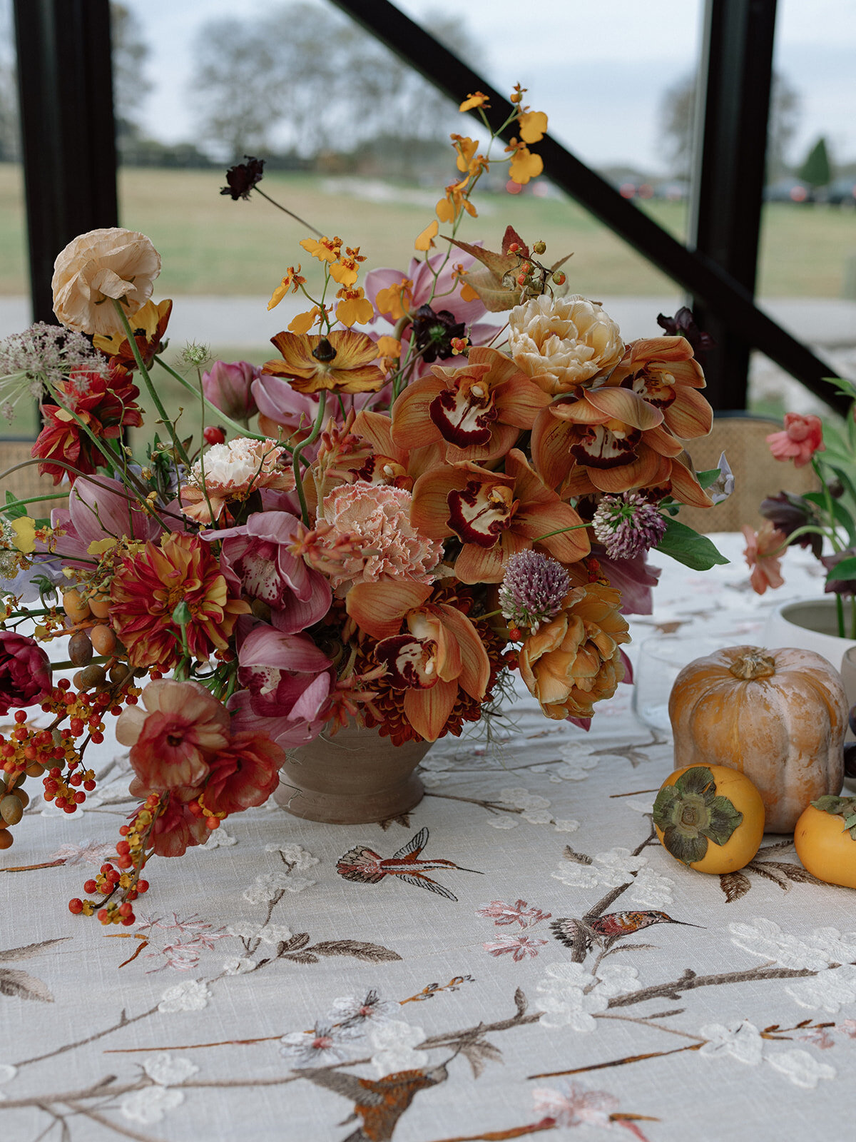 Clustered and styled floral arrangements, fruits, and art pieces for fall wedding reception. Low centerpieces mixed with ikebana arrangements and bud vases decorate the reception tables at this fall wedding. Floral centerpieces featuring orchids, ranunculus, sweet peas, and bittersweet. Styled wedding tables with fruits, curated candles, and floral arrangements. Tasteful fall color palette of copper, ruby, gold, burgundy, rust, and lavender. Design by Rosemary & Finch Floral Design in Nashville, TN.