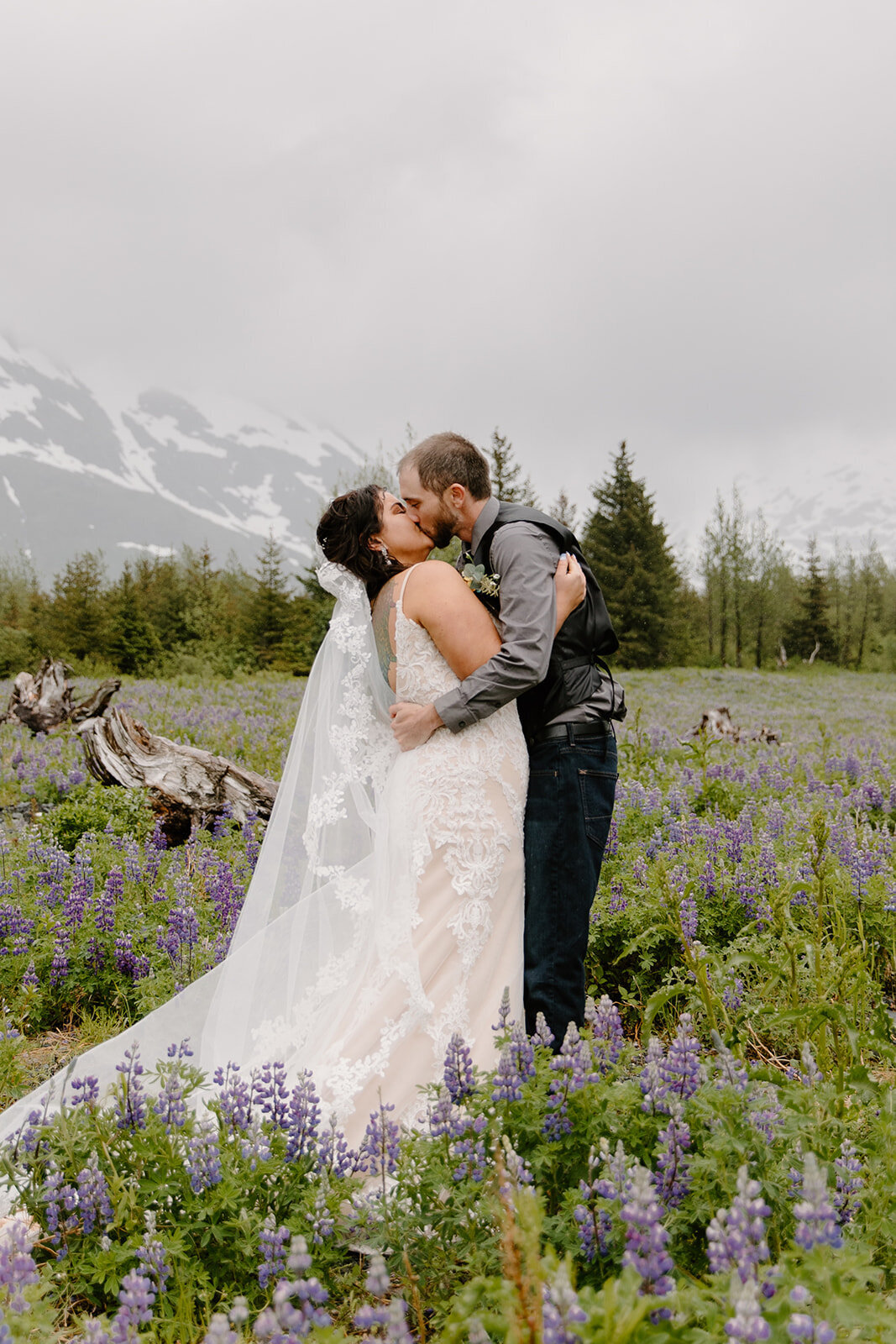 Elopement couple shares kiss by misty Alaska mountain and flowers..
