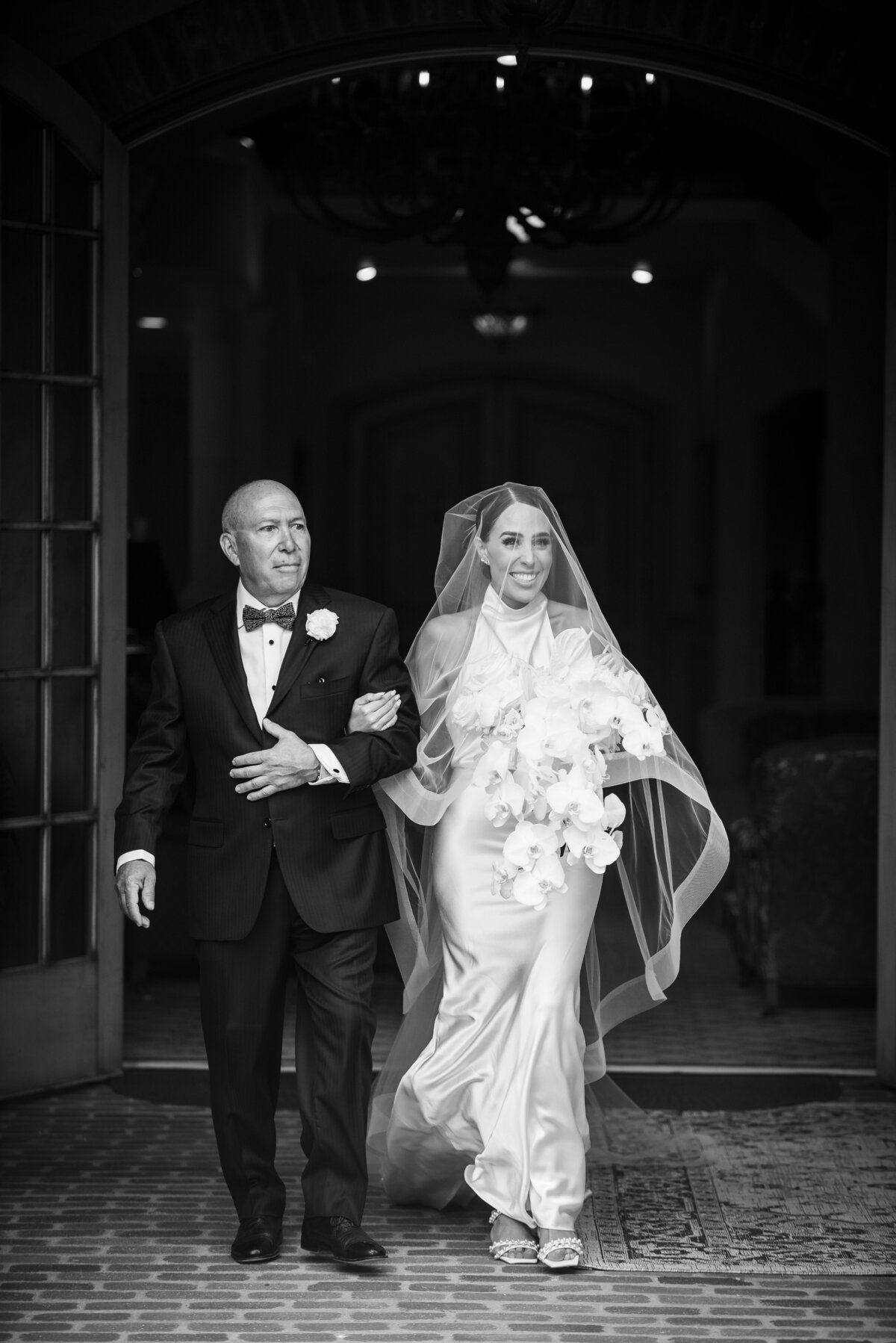 A candid moment of a bride walking up the aisle with her father with her veil draped over her face.