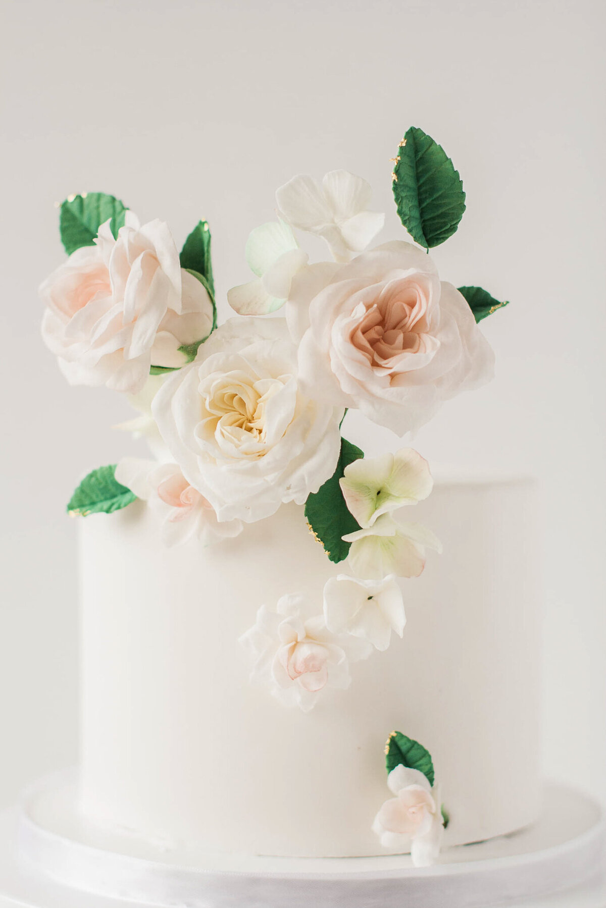 Simple and elegant one-tiered white wedding cake with life like sugar flowers, created by Brianne Gabrielle Cakes,  elegant cakes & desserts in Edmonton, AB, featured on the Brontë Bride Vendor Guide.