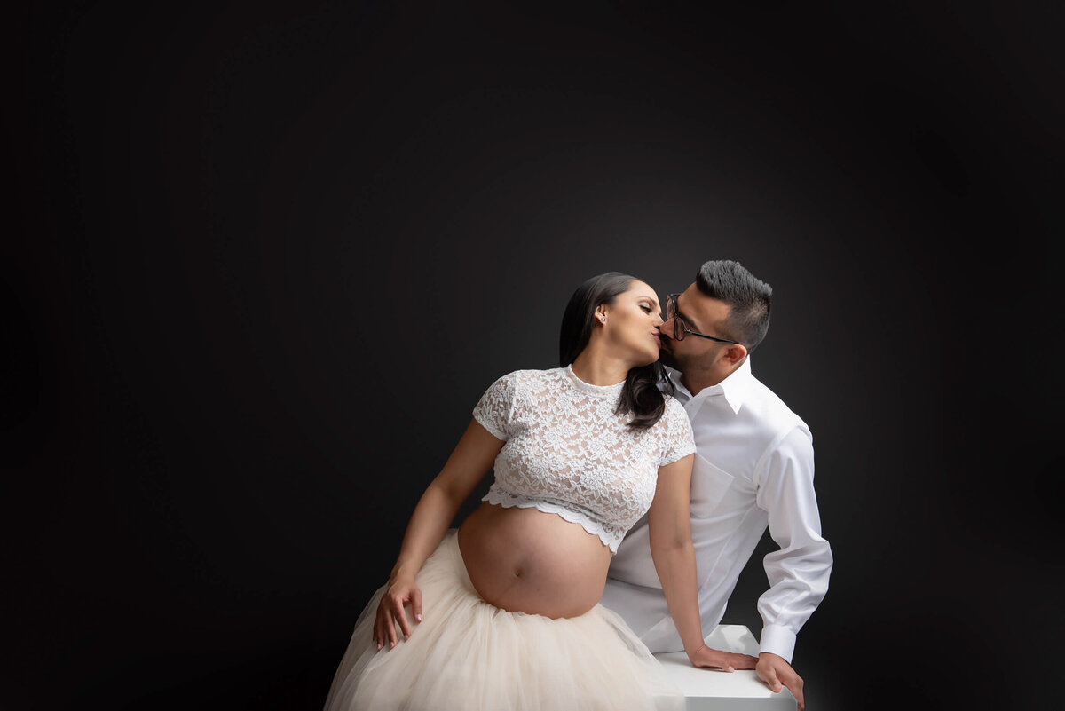 husband and white facing each other sitting on a white block for their studio maternity photos in Burlington, ON