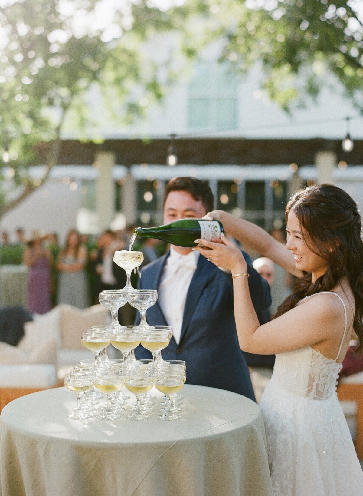 A joyful moment of a bride and groom pouring champagne into a tower of glasses during their elegant wedding celebration at Solage in Napa Valley, California. The stunning venue provides a luxurious backdrop for this classic and festive tradition