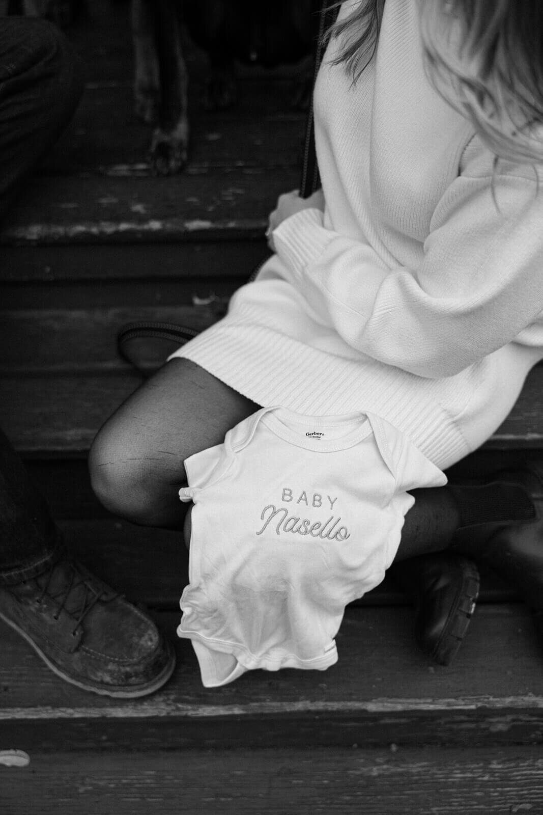 Woman sitting down with baby onesie on her lap for baby announcement photos in Finger Lakes, NY