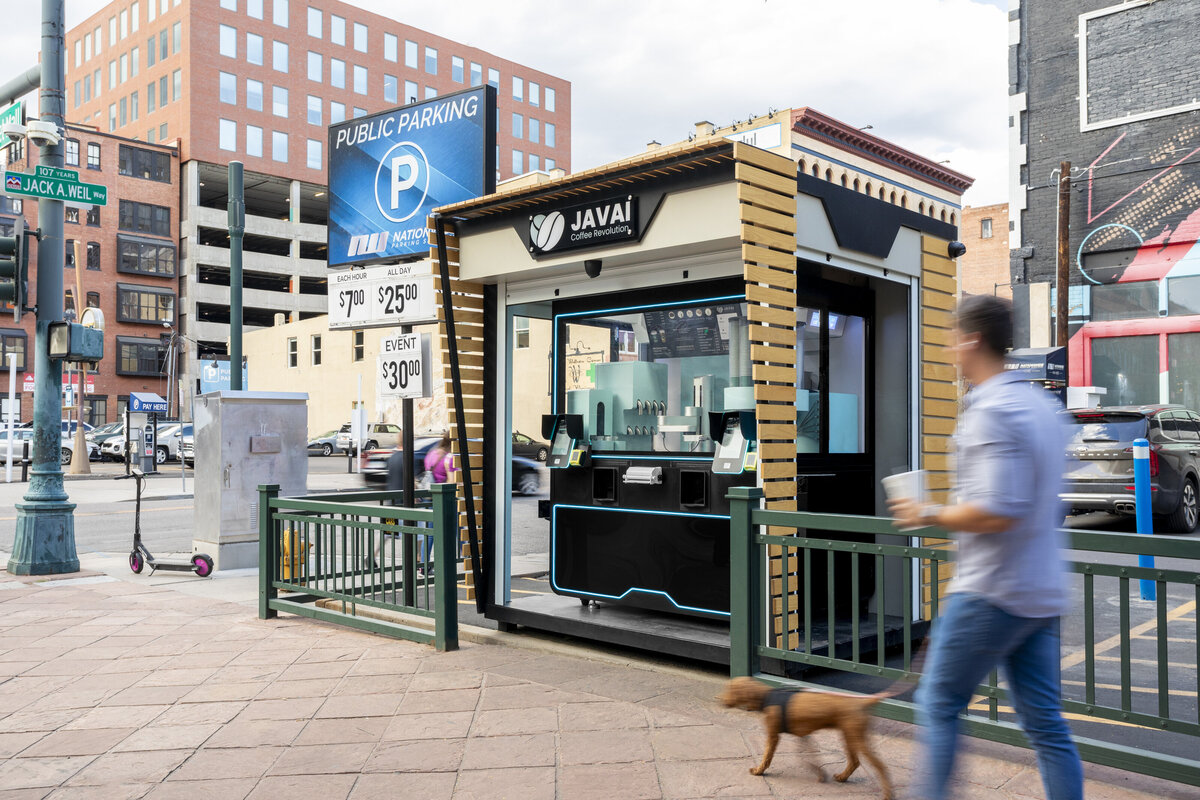 Javai coffee robotic barista vending machine on the corner of 16th street and Wazee street in downtown, Denver. Man and Dog walking in front of the machine with a coffee cup in hand.