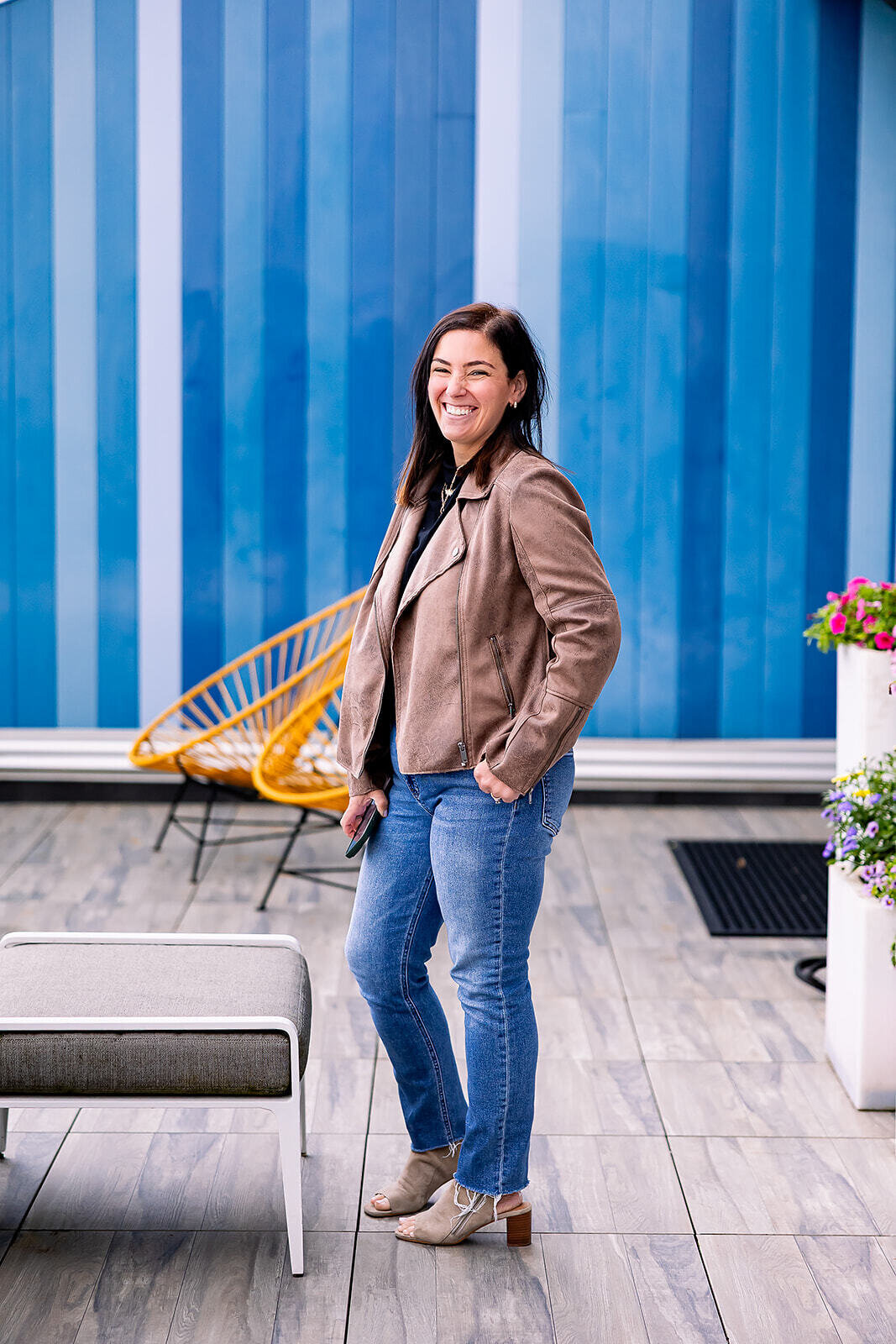 Becky wearing a light brown leather jacket while smiling on a colorful blue background