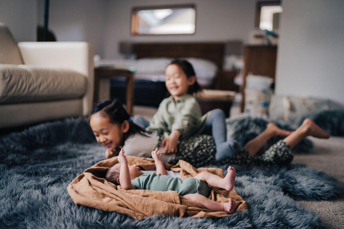 two-big-sisters-laughing-with-newborn-boy