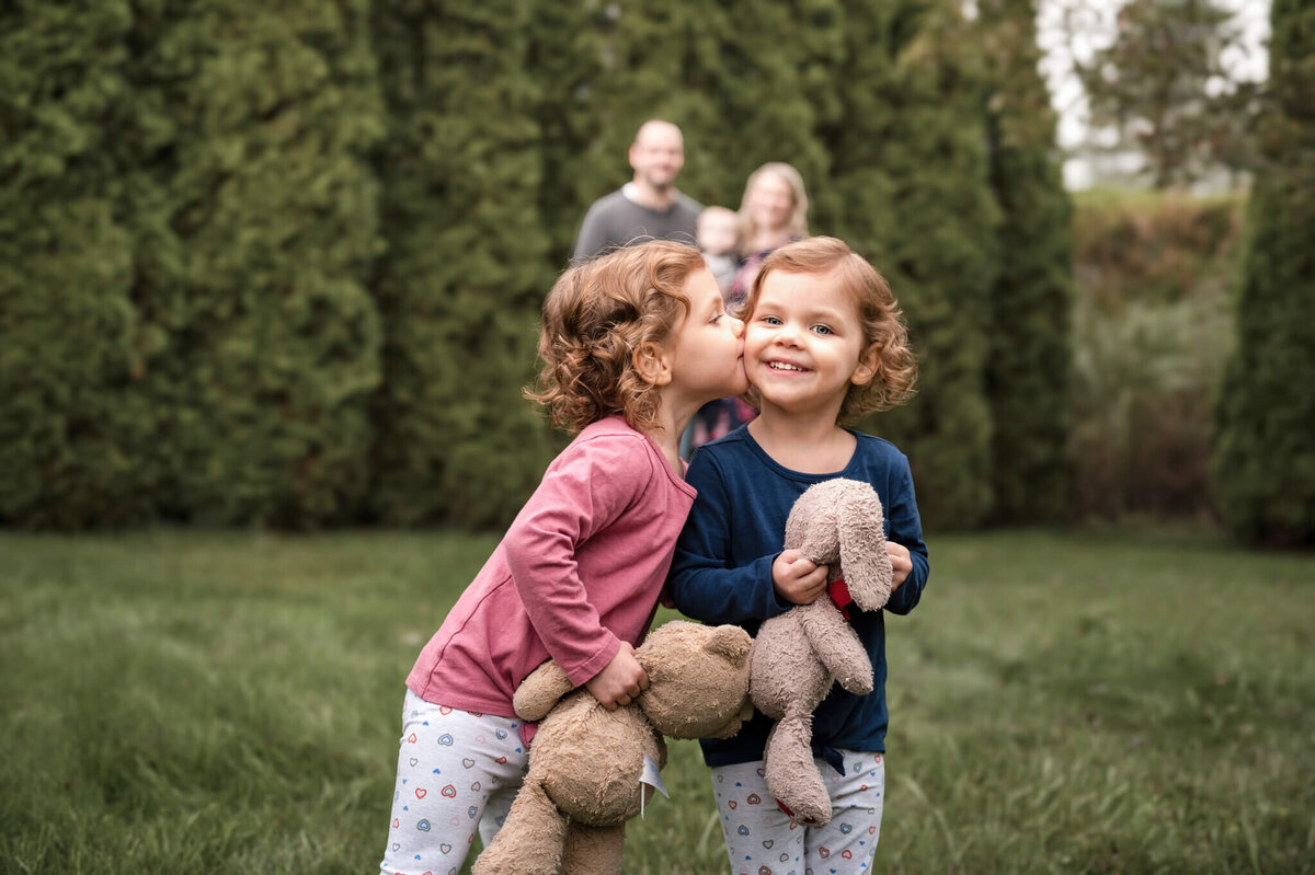 Siblings are in focus close to the camera, while parents are looking at them from way back.