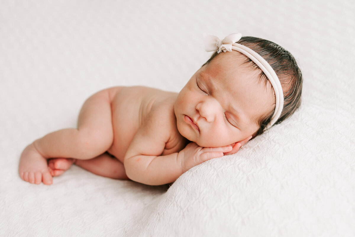 portrait of baby sleeping on white lacy blanket with her hands under her cheek