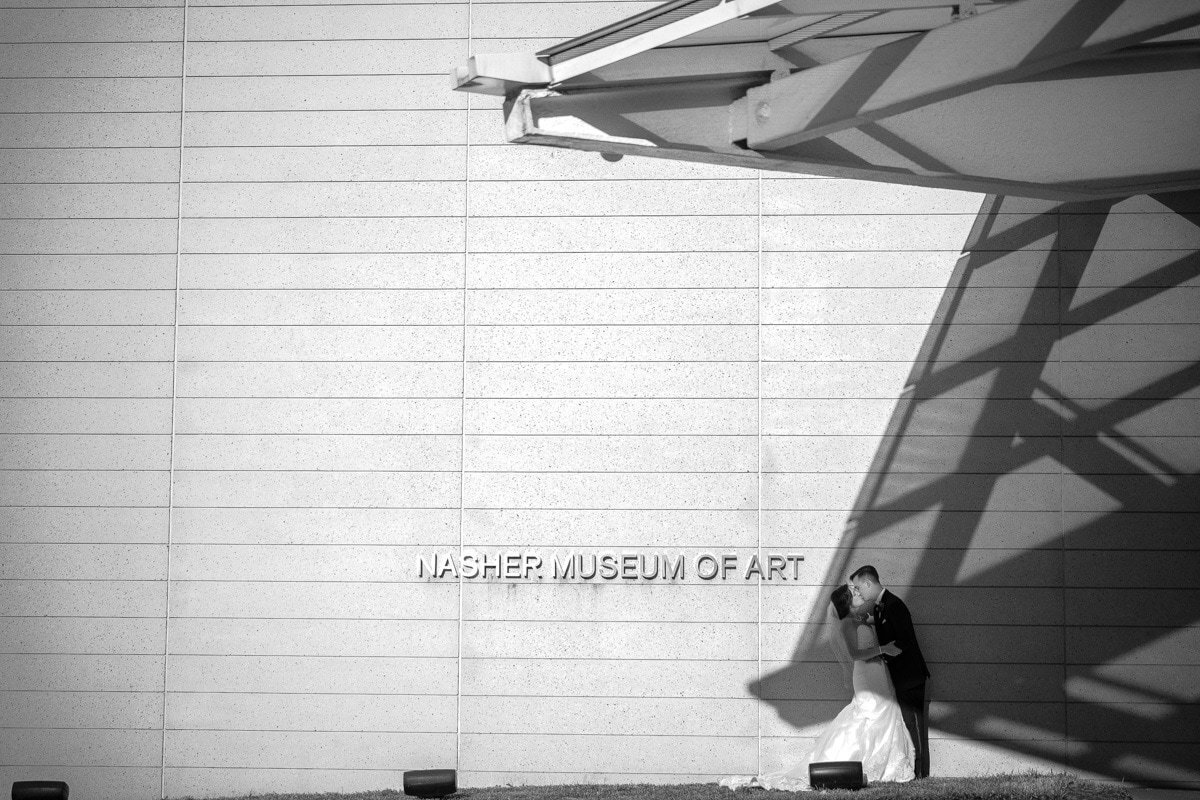 A wedding couple kissing outside an art museum .